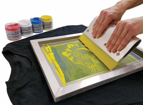 Person screen printing a design on a t-shirt with ink bottles in the background