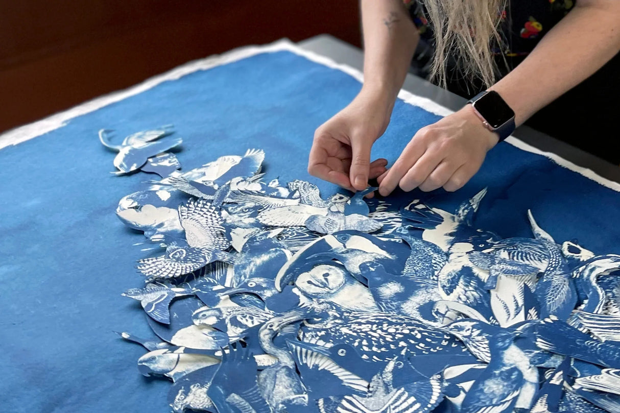 Person working on a blue fabric with white patterns, possibly assembling or arranging pieces of cyanotype images