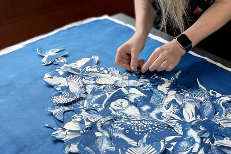 Person working on a blue fabric with white patterns, possibly assembling or arranging pieces of cyanotype images