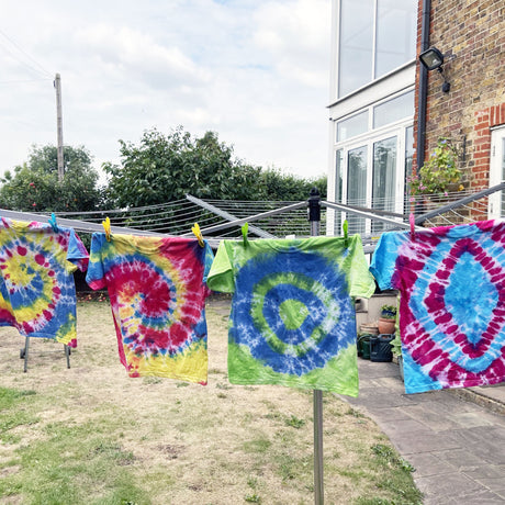 Colorful tie-dye shirts hanging on a clothesline outside a house.