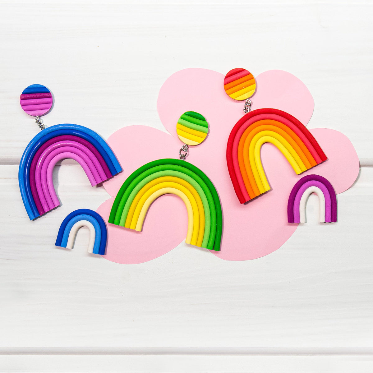 Colorful rainbow-shaped earrings made from Fimo on a pink cloud-shaped background