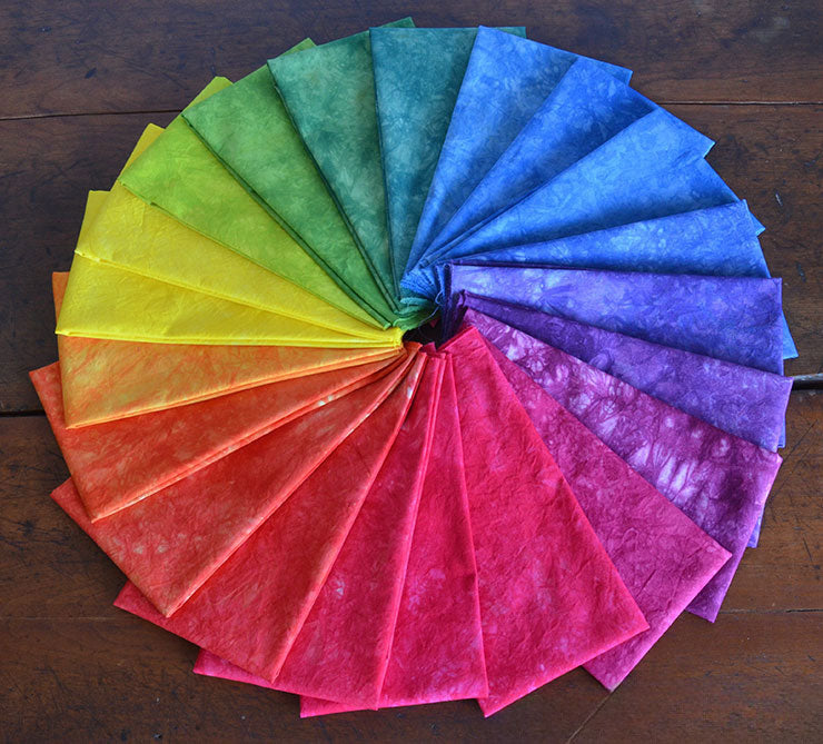 Fan of colorful fabric swatches arranged in a rainbow pattern on a wooden surface.