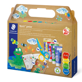 Staedtyler Noris Junior children's activity kit in a brown cardboard carrying box with colorful illustrations, including a green frog, blue clouds, paint tubes, scissors, and small activity cards.
