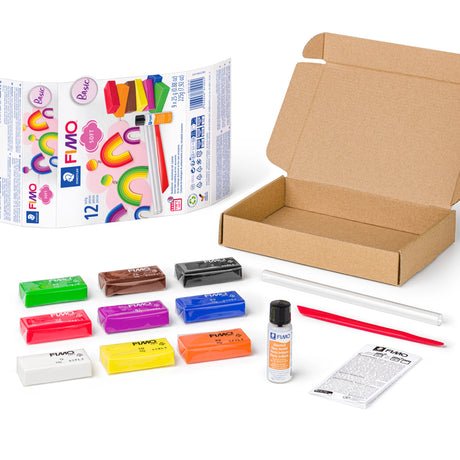 Fimo clay kit with multiple colorful clay sticks, a cardboard box, a tube of liquid activator, a plastic spatula, and an instruction booklet on a white background.