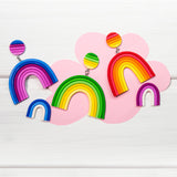Colorful rainbow-shaped earrings made from Fimo on a pink cloud-shaped background