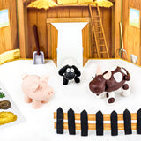 Fimo small farm-themed toy figurines—a pink pig, a black sheep, and a brown-and-white cow—placed on a white surface in front of a miniature wooden barn scene with a fence in the foreground.