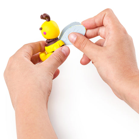 A pair of hands holding a Fimo polymer clay bee model against a plain white background.