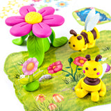 A colorful children's toy scene with two yellow bumblebee figures made from Fimo on a printed green mat with floral illustrations.