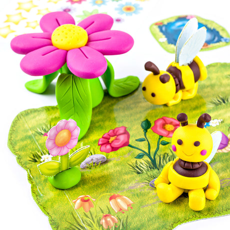 A colorful children's toy scene with two yellow bumblebee figures made from Fimo on a printed green mat with floral illustrations.