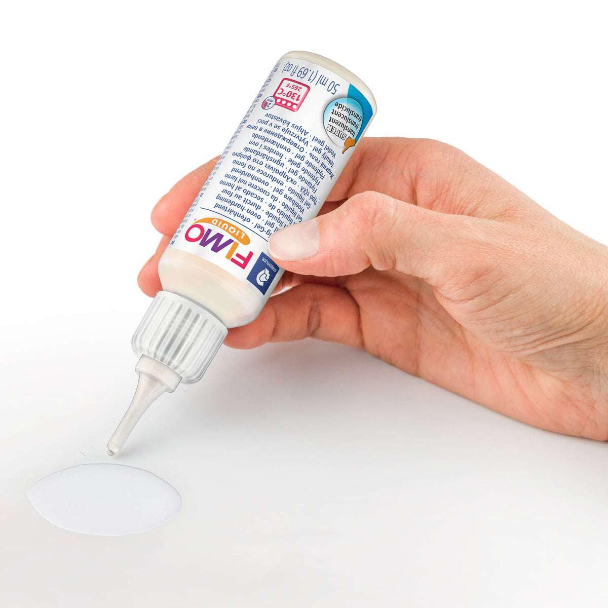 A hand holds a white bottle of Fimo White modeling clay, dispensing a small puddle of white clay onto a white surface against a white background.