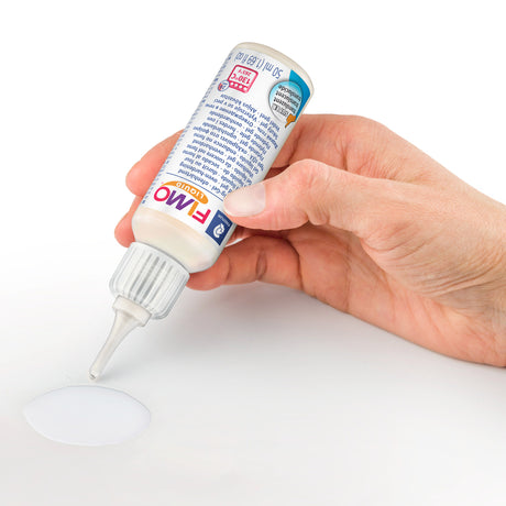 A hand holds a white bottle of Fimo White modeling clay, dispensing a small puddle of white clay onto a white surface against a white background.