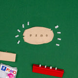 A top-down view of a FIMO clay modeling set on a green felt surface. The main product is a beige clay sheet in the center spelling 'FIMO', surrounded by small white tiles.