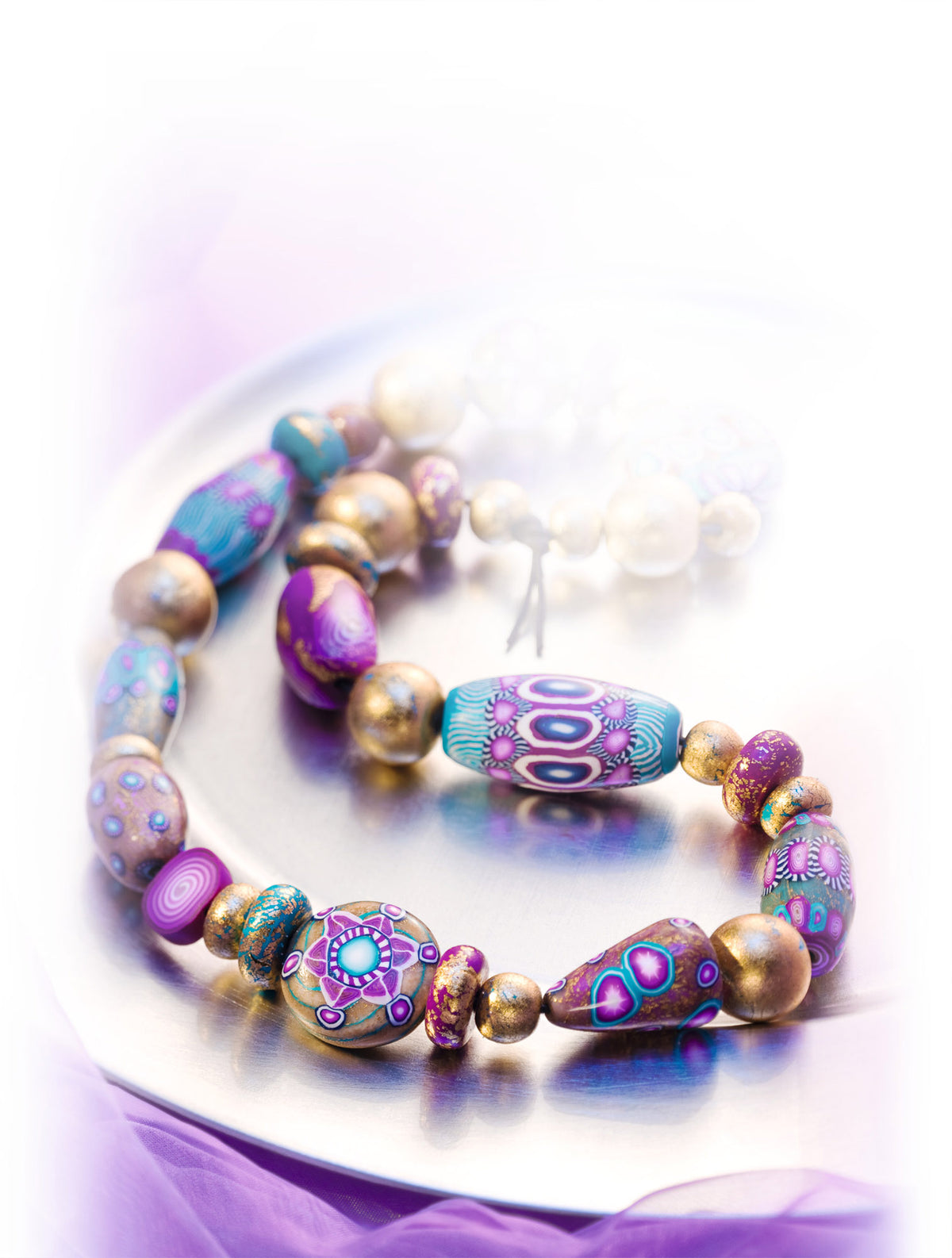A Fimo Professional Polymer Clay beaded bracelet with colourful patterned beads in purple, blue, teal, and metallic gold, displayed on a reflective silver plate with a soft purple glow.