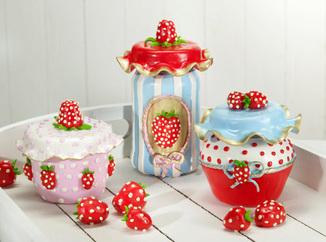 Three decorative fimo polymer clay  strawberry-themed jars styled like cupcakes, arranged on a white wooden surface against a white paneled background.