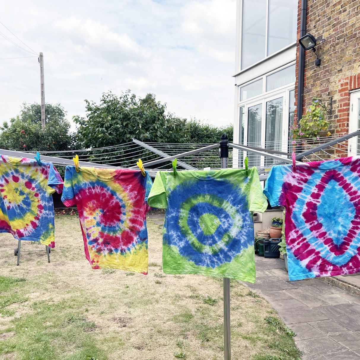 Colorful tie-dye shirts hanging on a clothesline outside a house.